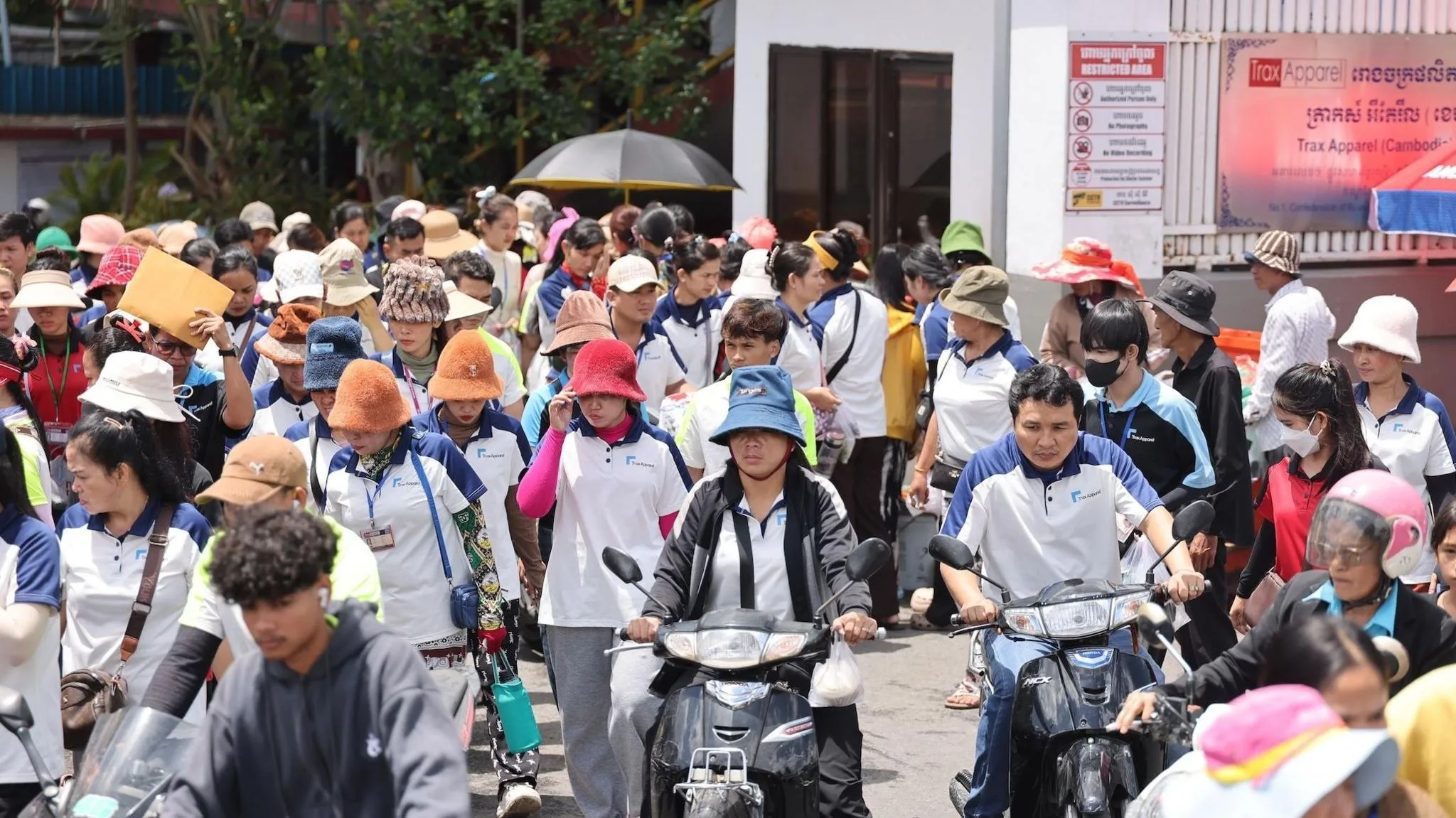 A large group of workers are leaving Trax Apparel, some on motorbikes.