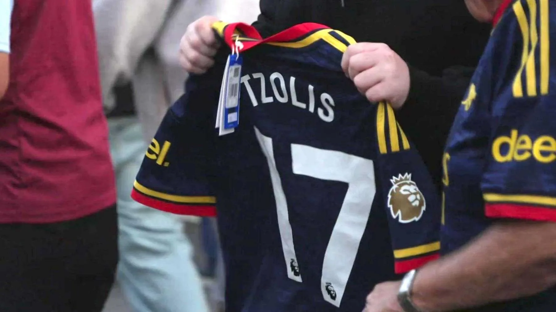 A fan holds up a brand new Arsenal away shirt with 'Tzolis' on the back and the shop label still attached.