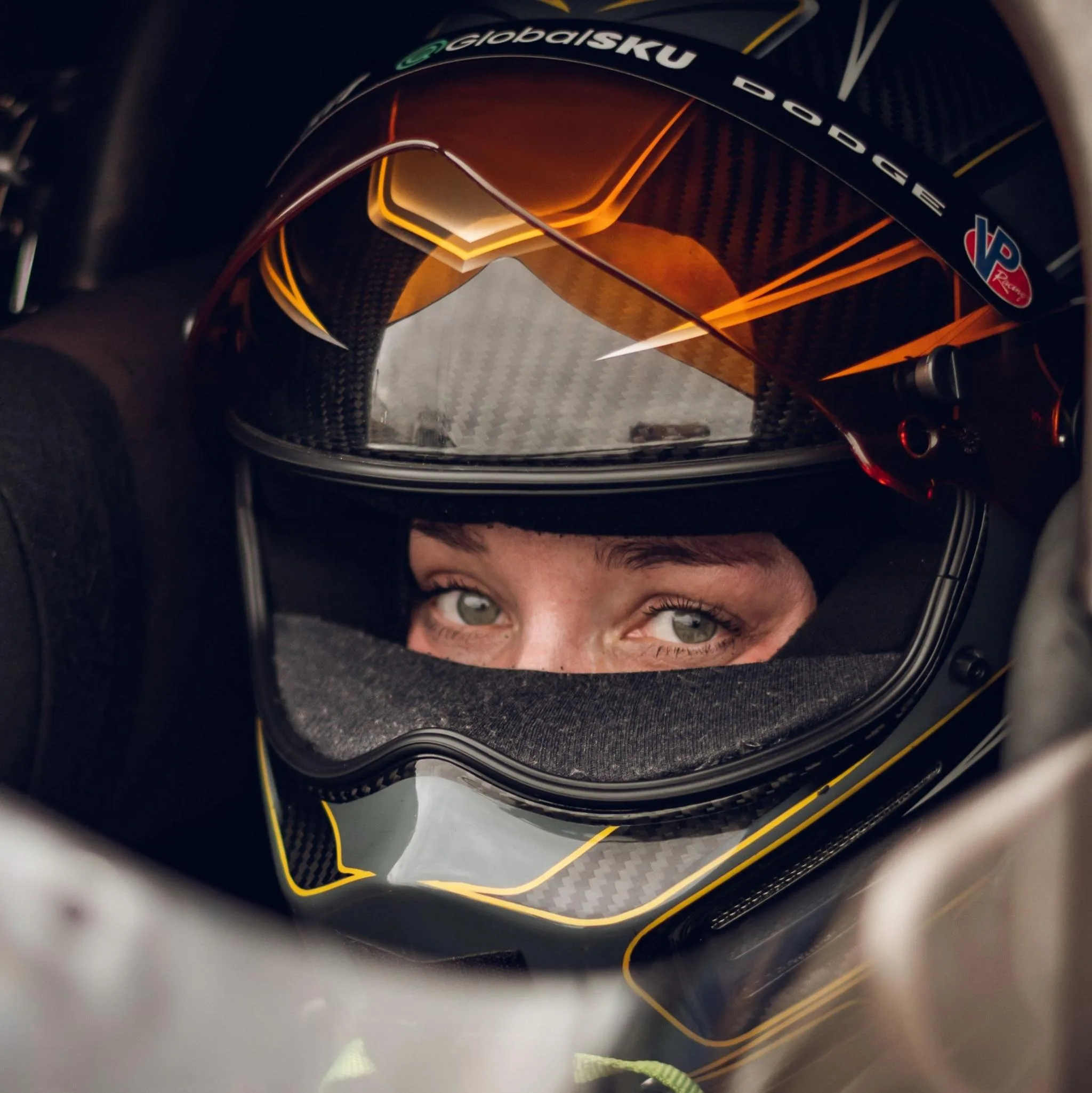 Swedish Top Fuel drag racing driver Susanne Callin wearing a black and orange racing helmet with just her eyes exposed through the visor, looking directly at the camera, taken at Mantorp in Sweden in 2025.