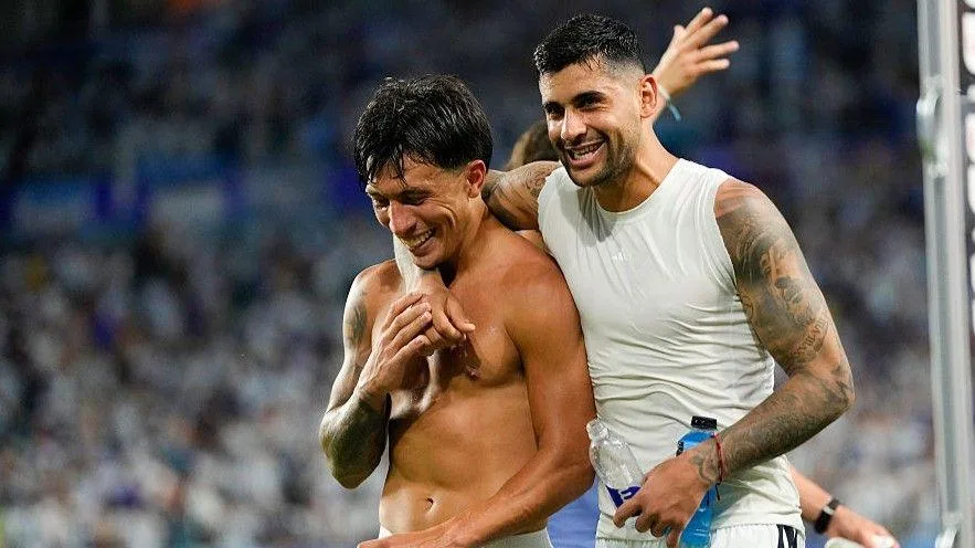 Argentina team-mates Lisandro Martinez, who is topless, and Cristian Romero, who is wearing a vest. Romero has an arm around Martinez as both smile