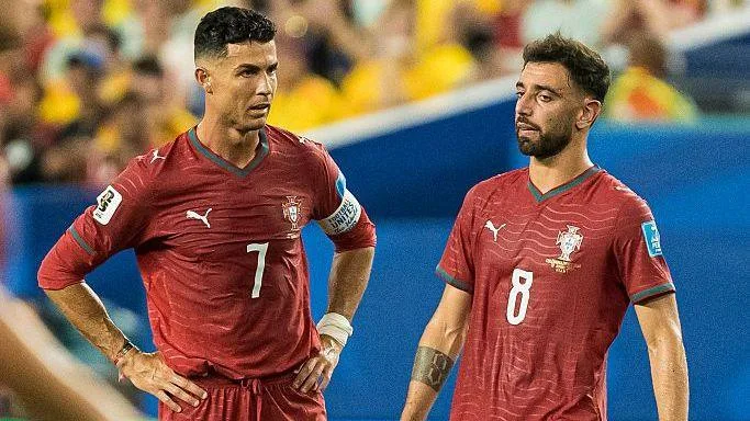 Cristiano Ronaldo and Bruno Fernandes stand close together as they wear Portugal's scarlet red kit