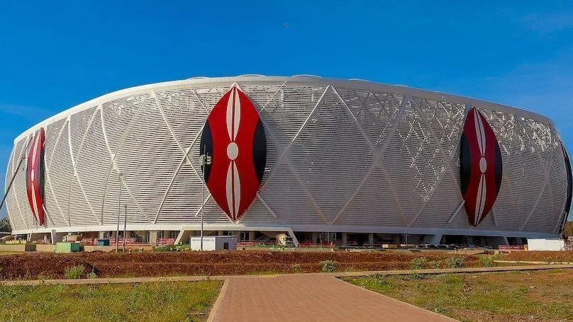 Exterior of a football stadium showing three Kenyan shields in red, white and black on top of a white wrap around