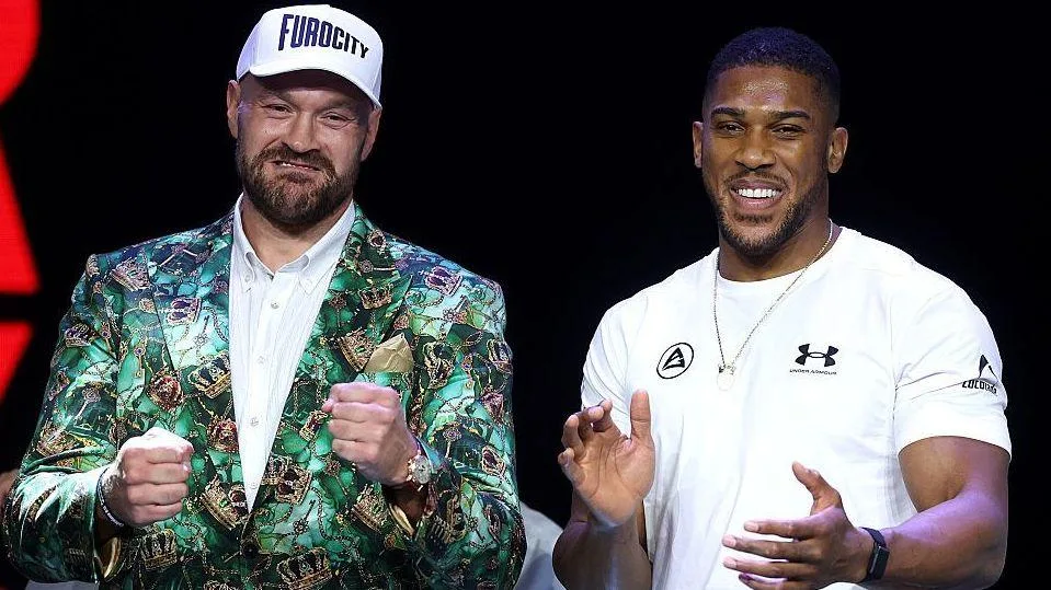 Tyson Fury holds up his fists and Anthony Joshua holds up his hands and smiles