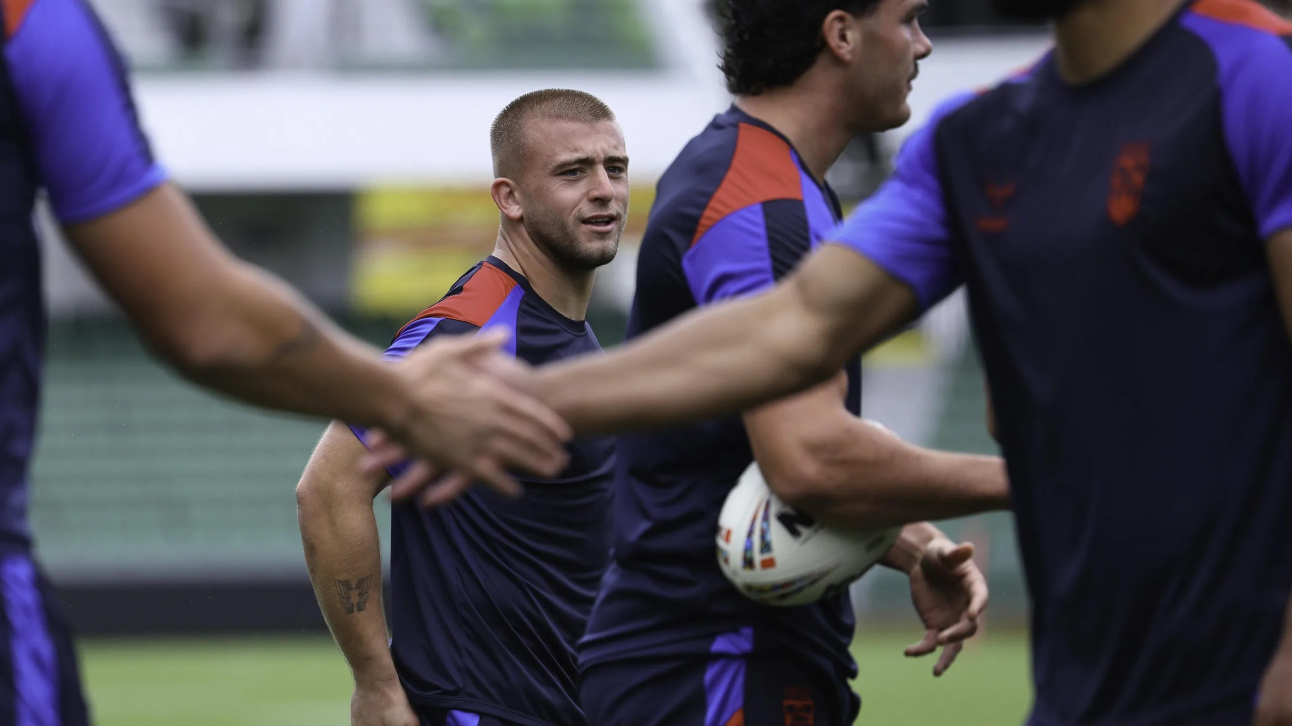 Mikey Lewis looks on during a training session, as two team-mates shake hands in the foreground