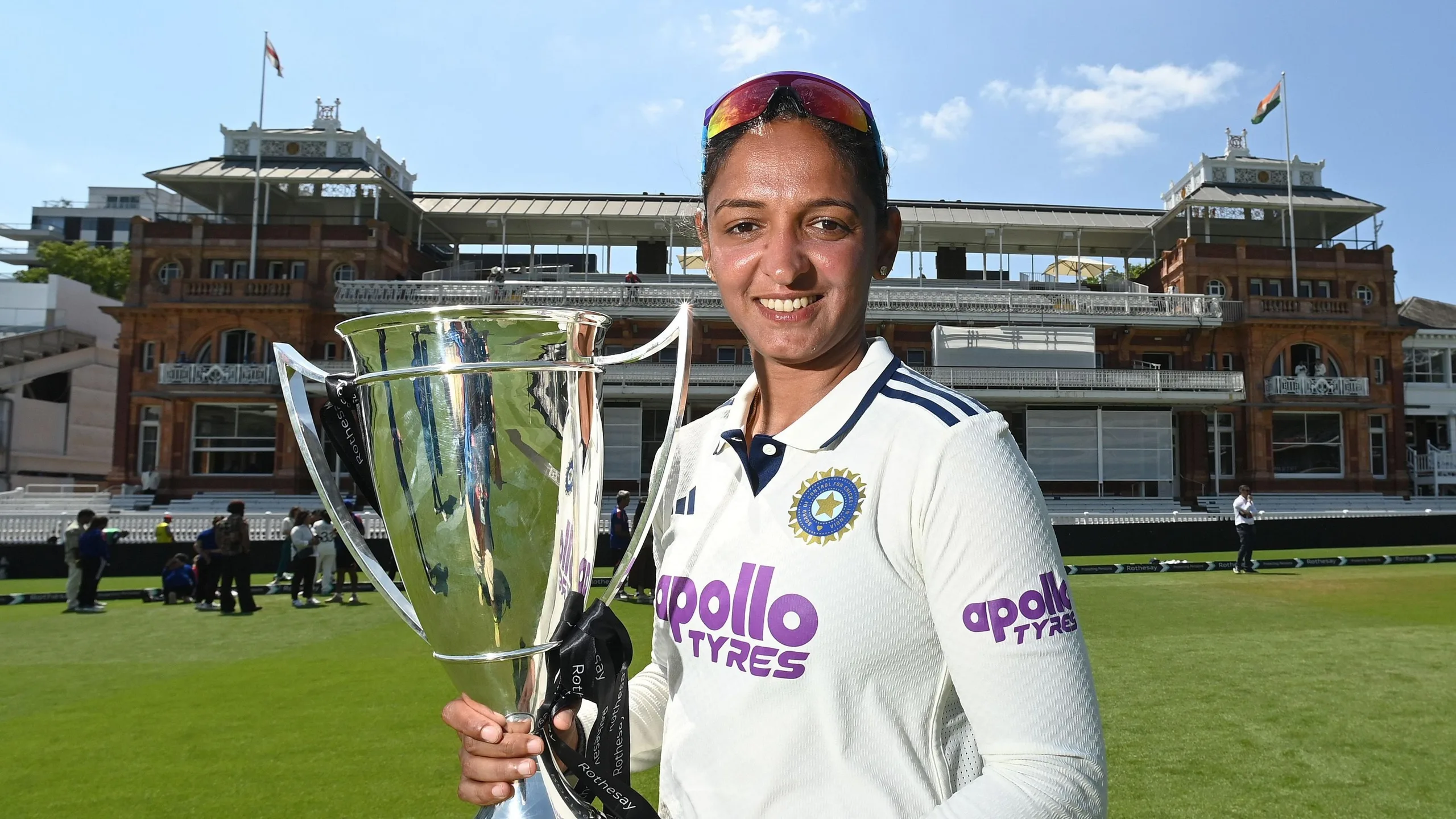 Harmanpreet Kaur, wearing cricket whites and holding a trophy, standing in front of the Lord's pavilion