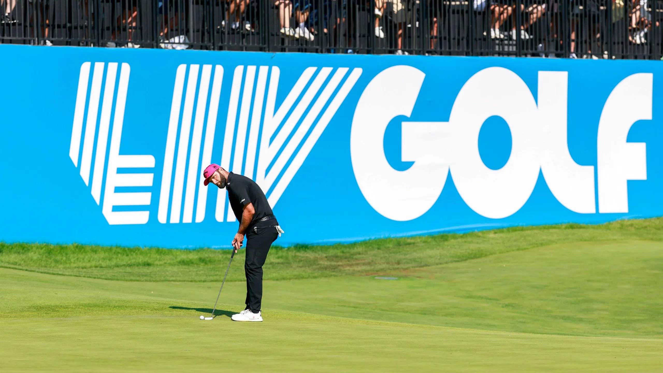 Jon Rahm playing a shot in front of a large banner saying LIV Golf
