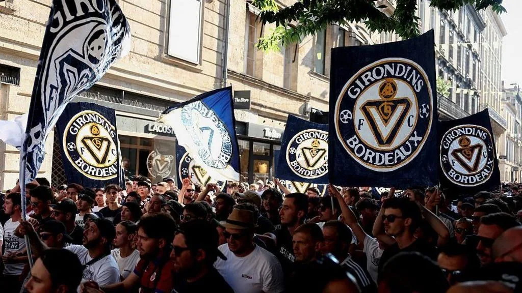 Bordeaux fans protest as they carry banners bearing the club's badge