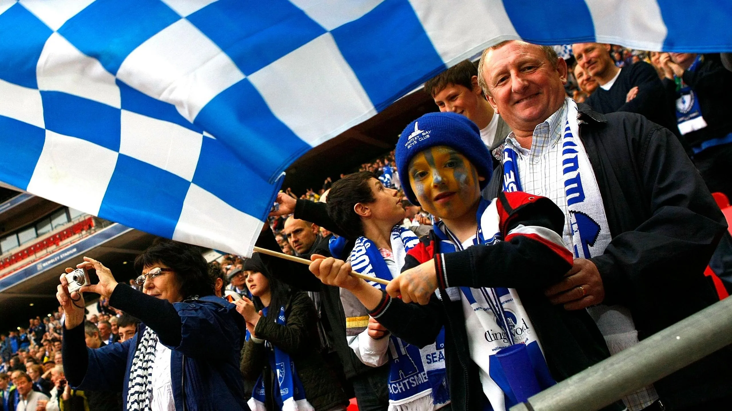 Whitley Bay fans wearing the club's blue and white colours and waving a flag