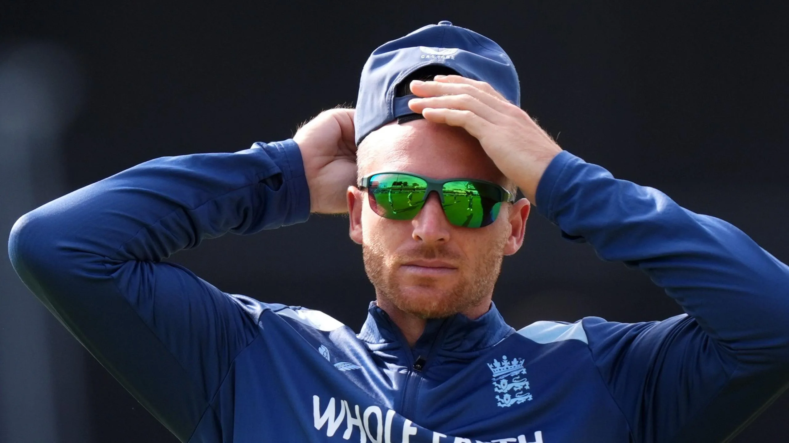 Jos Buttler rubs his head, while wearing sunglasses and a cap