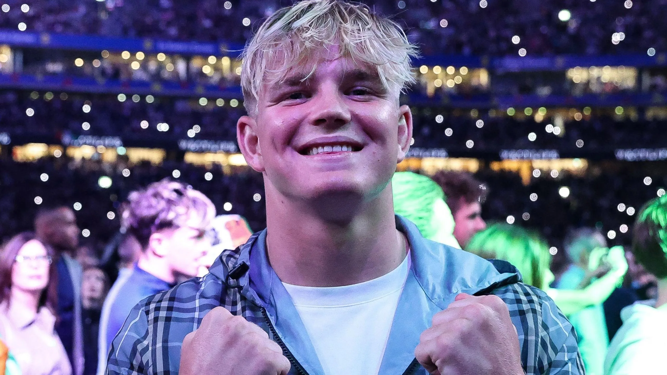 A smiling Henry Pollock is pictured in casual wear - white T-shirt and hooded top - with lights in the stands behind him as he attends Croke Park for Katie Taylor's final boxing fight