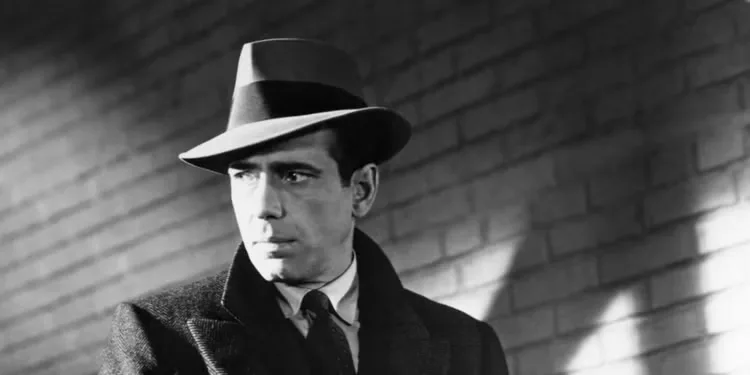 Humphrey Bogart as Sam Spade wearing a hat, trenchcoat, and tie in 'The Maltese Falcon'.