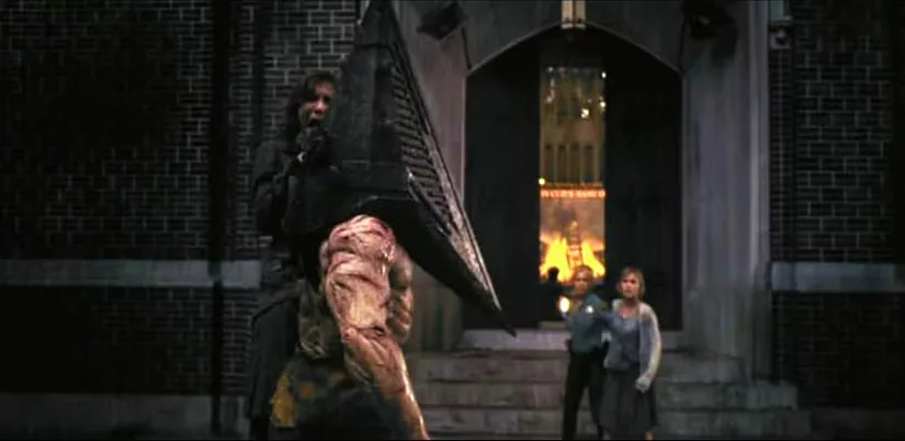 A male figure with a large pyramid for a head holds a woman up by the throat as two women watch in the background in Silent Hill (2006)