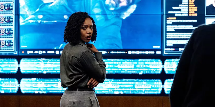 Naomi Ackie's character is standing in front of a giant screen, turning to look over her shoulder in concern.