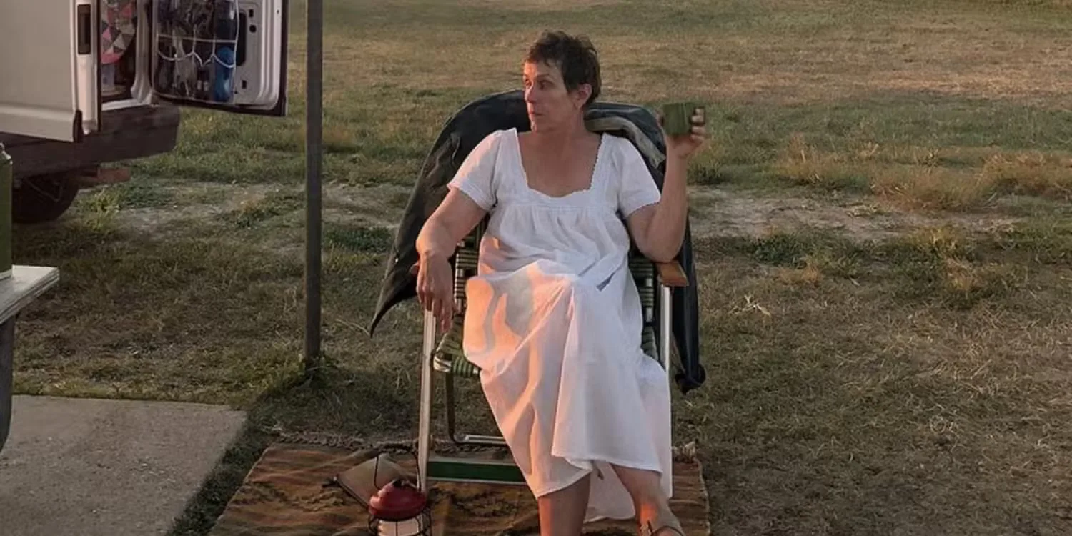 Frances McDormand in a nightgown sitting on a chair and holding a mug in Nomadland