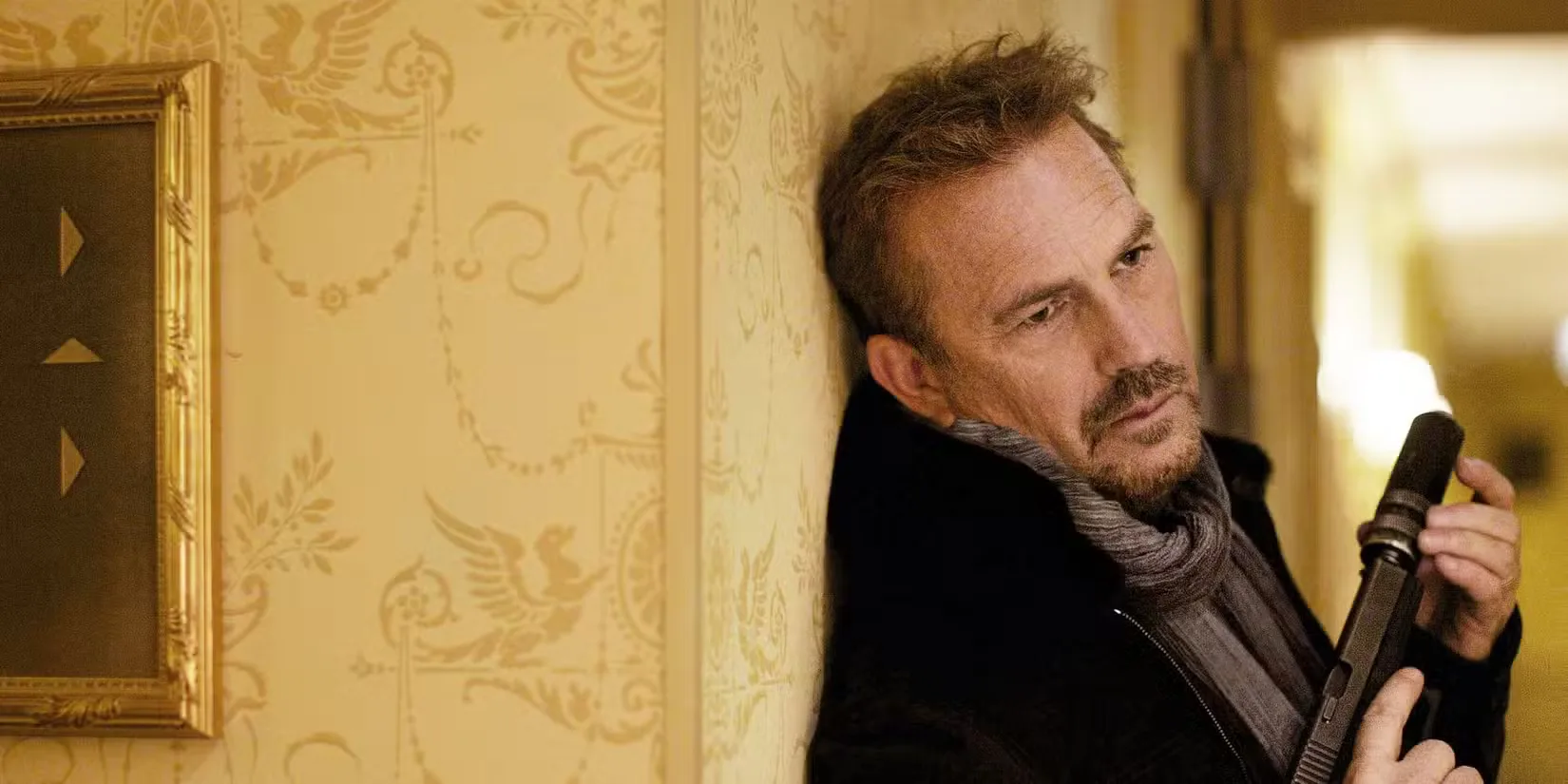 Kevin Costner holds a gun and leans against a wall in '3 Days to Kill' (1)