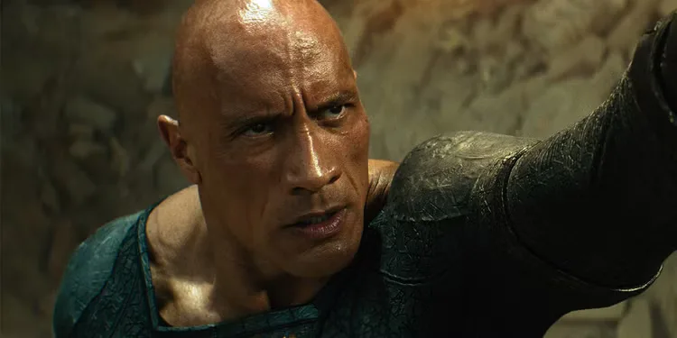 Dwayne Johnson scowls while lifting someone off camera in Black Adam.