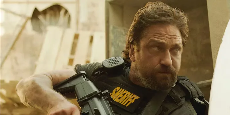 Gerard Butler as Big Nick holding a gun and ducking in Den of Thieves (2018).