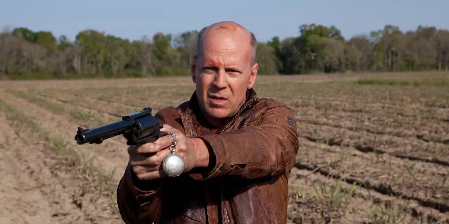 Bruce Willis pointing a gun in a field in Looper