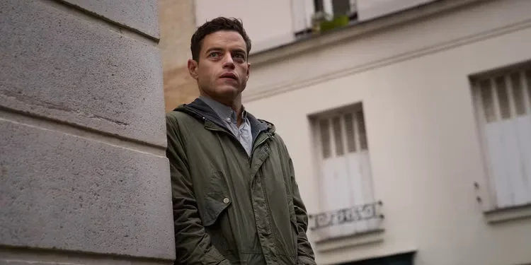 Rami Malek peeking around a building in The Amateur