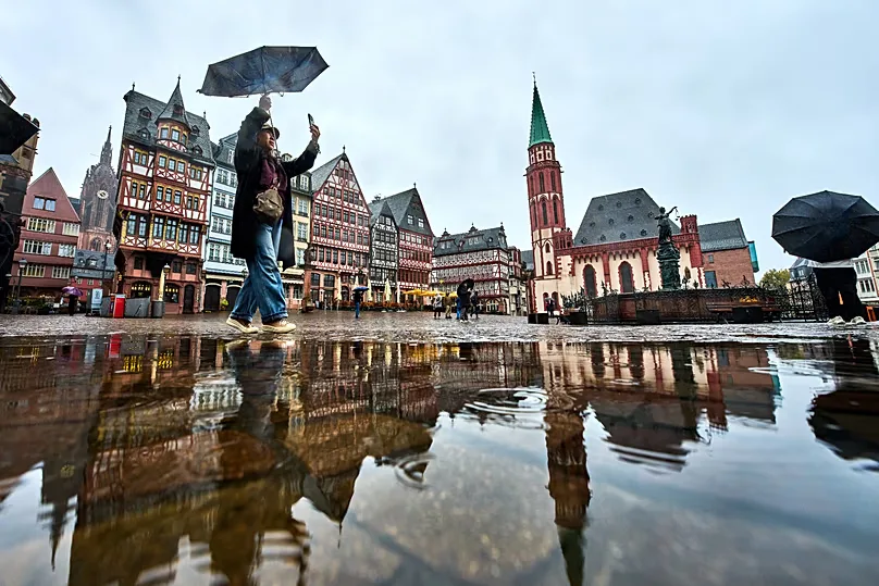 A tourist takes pictures on the Roemerberg square in Frankfurt, Germany, during rain falls on Sunday, Oct. 25, 2026. (AP Photo/Michael Probst)