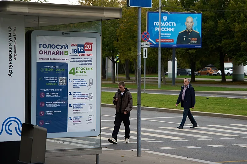 A poster advertising online voting in the elections; in the background a billboard shows a soldier with the slogan 