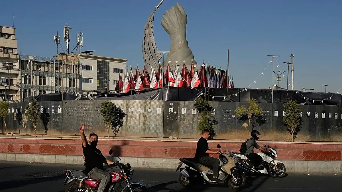 A man reacts to the camera while driving past a monument showing the clenched fist of the late Iranian Supreme Leader Ayatollah Ali Khamenei, who was killed in the US and