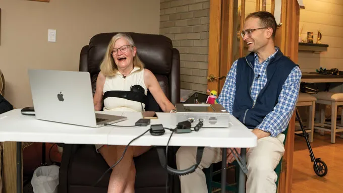 A woman hooked up to a computer smiles as she sits next to a male scientist.