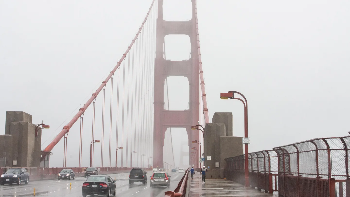 Vehicles and pedestrians cross the Golden Gate Bridge on a foggy damp-looking day.